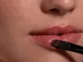 Labios con brillo y un pincel aplicando iluminador en el arco de cupido para un toque radiante.
