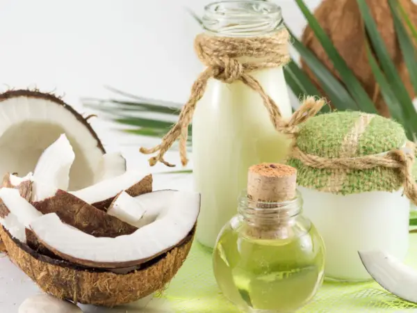 Aceite de coco para el pelo en frascos y botellas, junto a cocos frescos y hojas verdes.