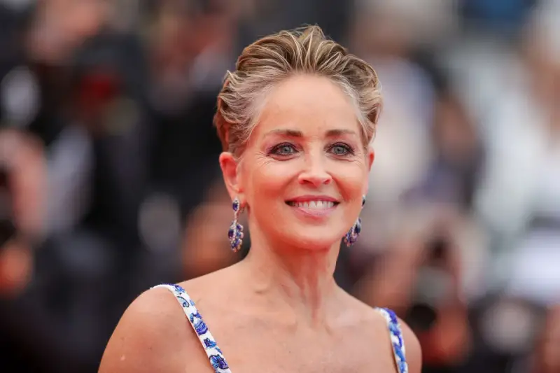 Sharon Stone luce un elegante corte bixie, con pendientes de zafiro y un vestido blanco con detalles azules.