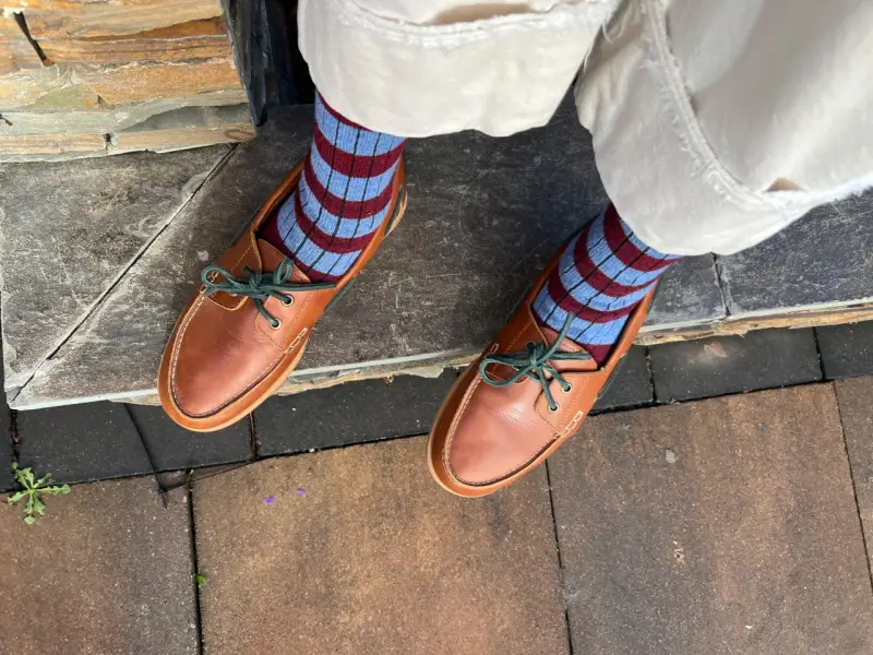 Pies con calcetines a rayas azul y burdeos y mocasines de cuero marrón. Un ejemplo de cómo combinar color teja ropa con estilo.
